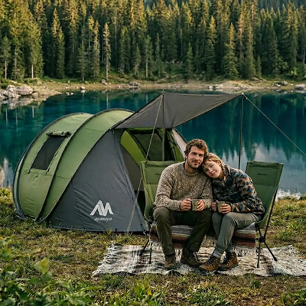Two people sitting in front of a green tent by a lake with trees in the background